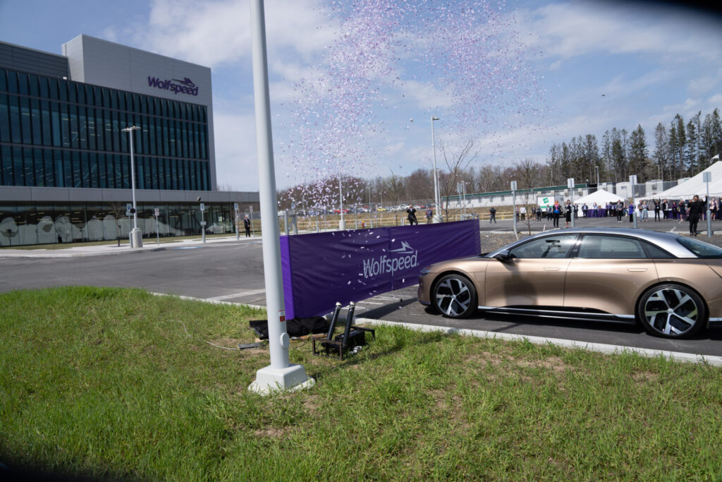 Landscape photo of a champagne colored electric vehicle being used to cut the ribbon on Wolfspeed's newest facility.